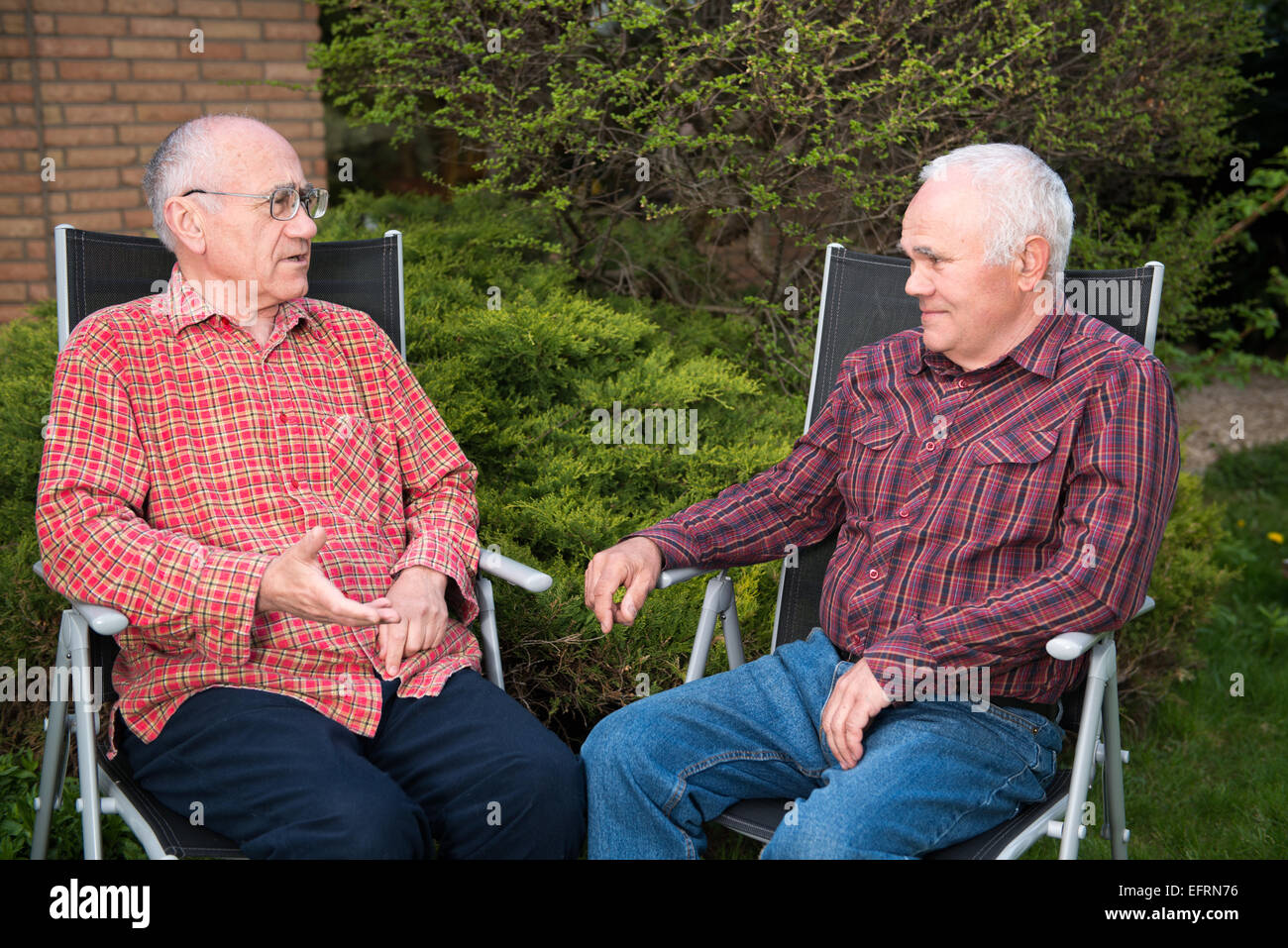 two senior men sitting in garden and chatting Stock Photo