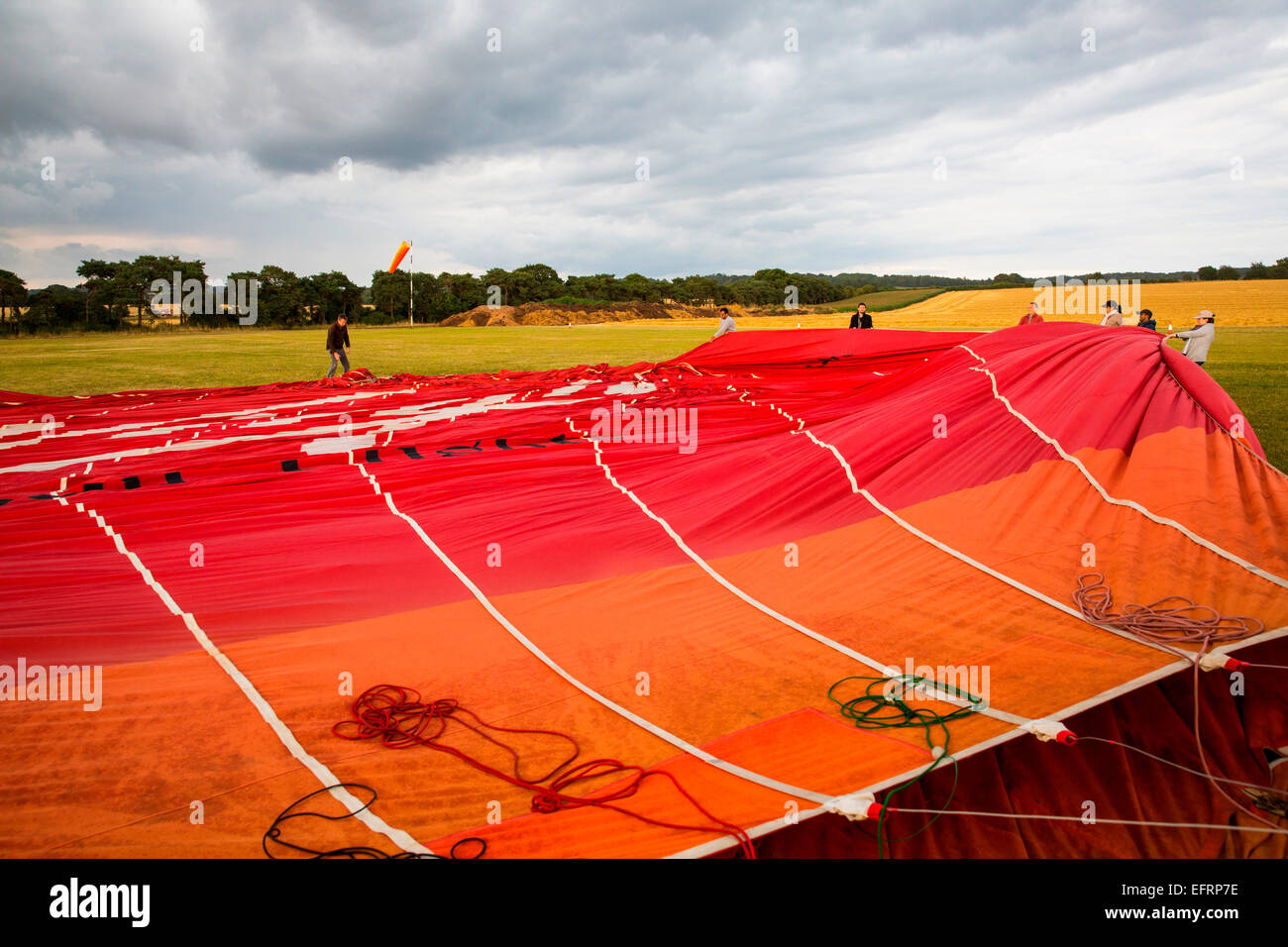 Crew unfurling red hot air balloon envelope on airfield, South Oxfordshire, England Stock Photo