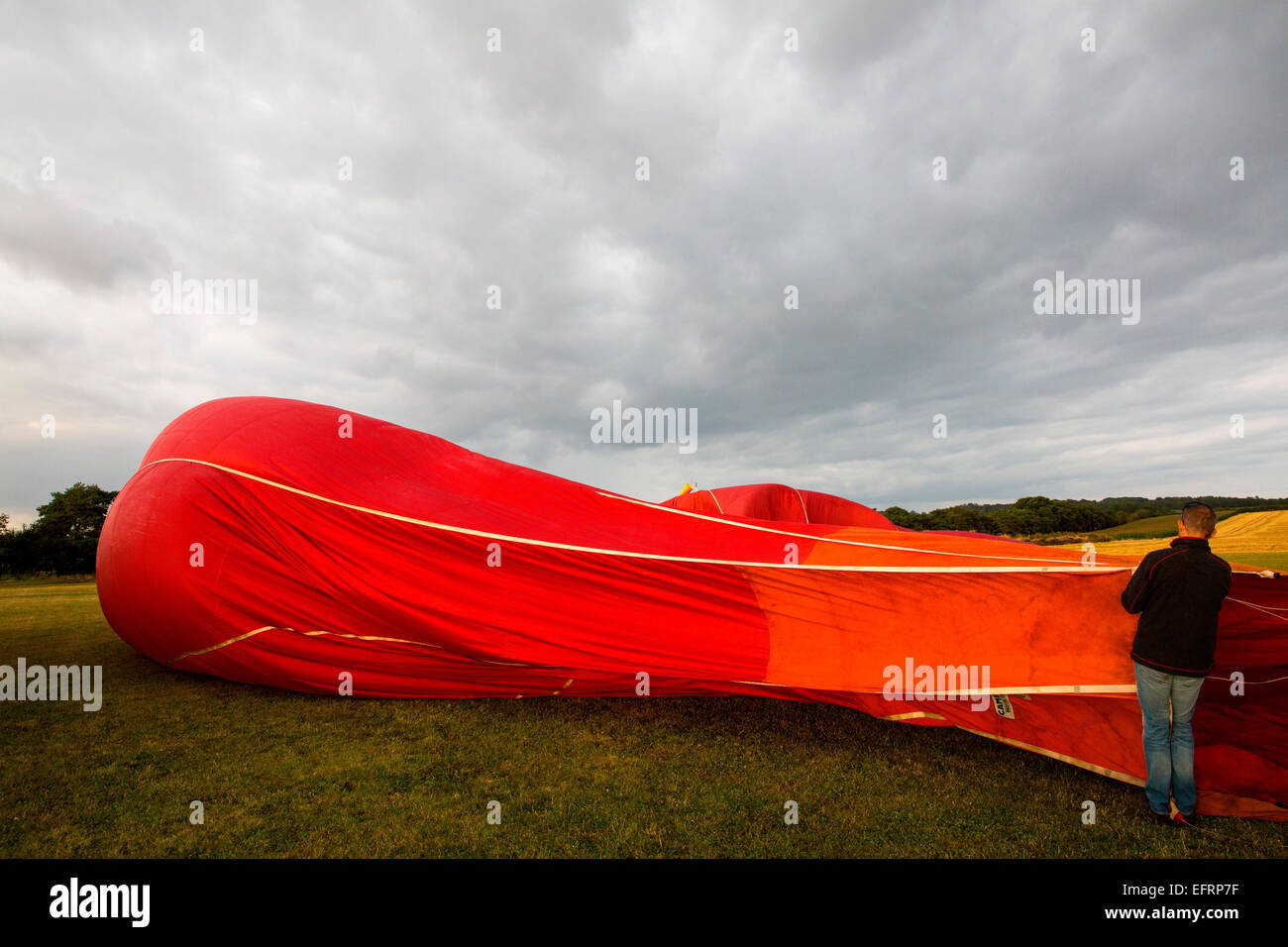 Male balloonist inflating red hot air balloon in field, South Oxfordshire, England Stock Photo