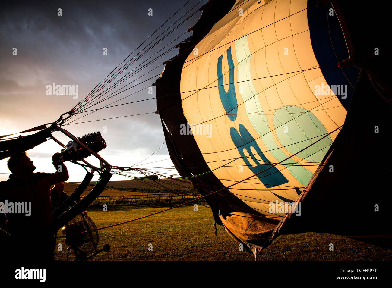 Man inflating hot air balloon at sunset, South Oxfordshire, England Stock Photo