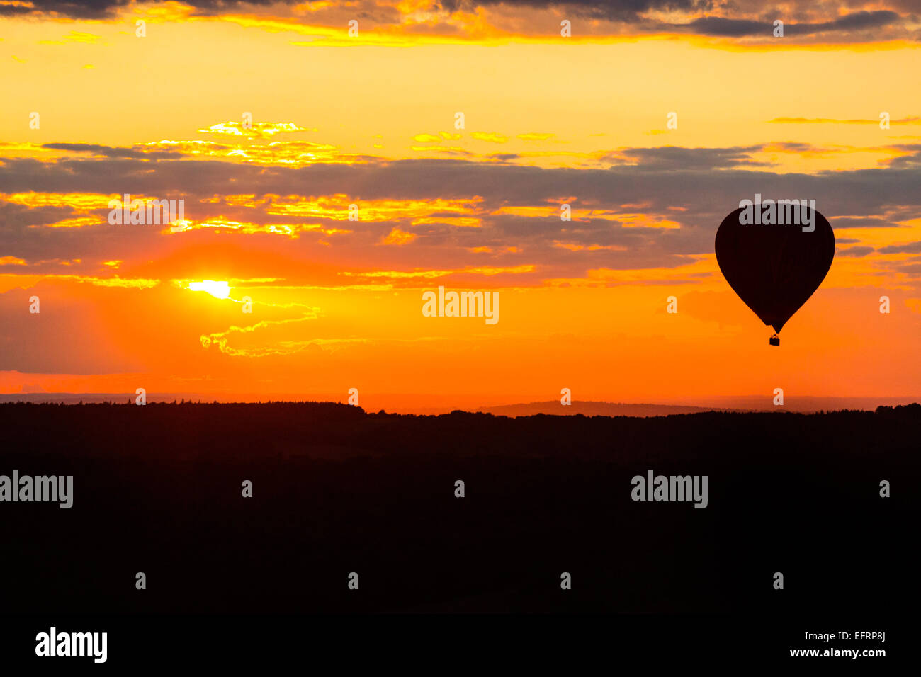 Silhouetted hot air balloon floating in dramatic golden sunset sky, Oxfordshire, UK Stock Photo