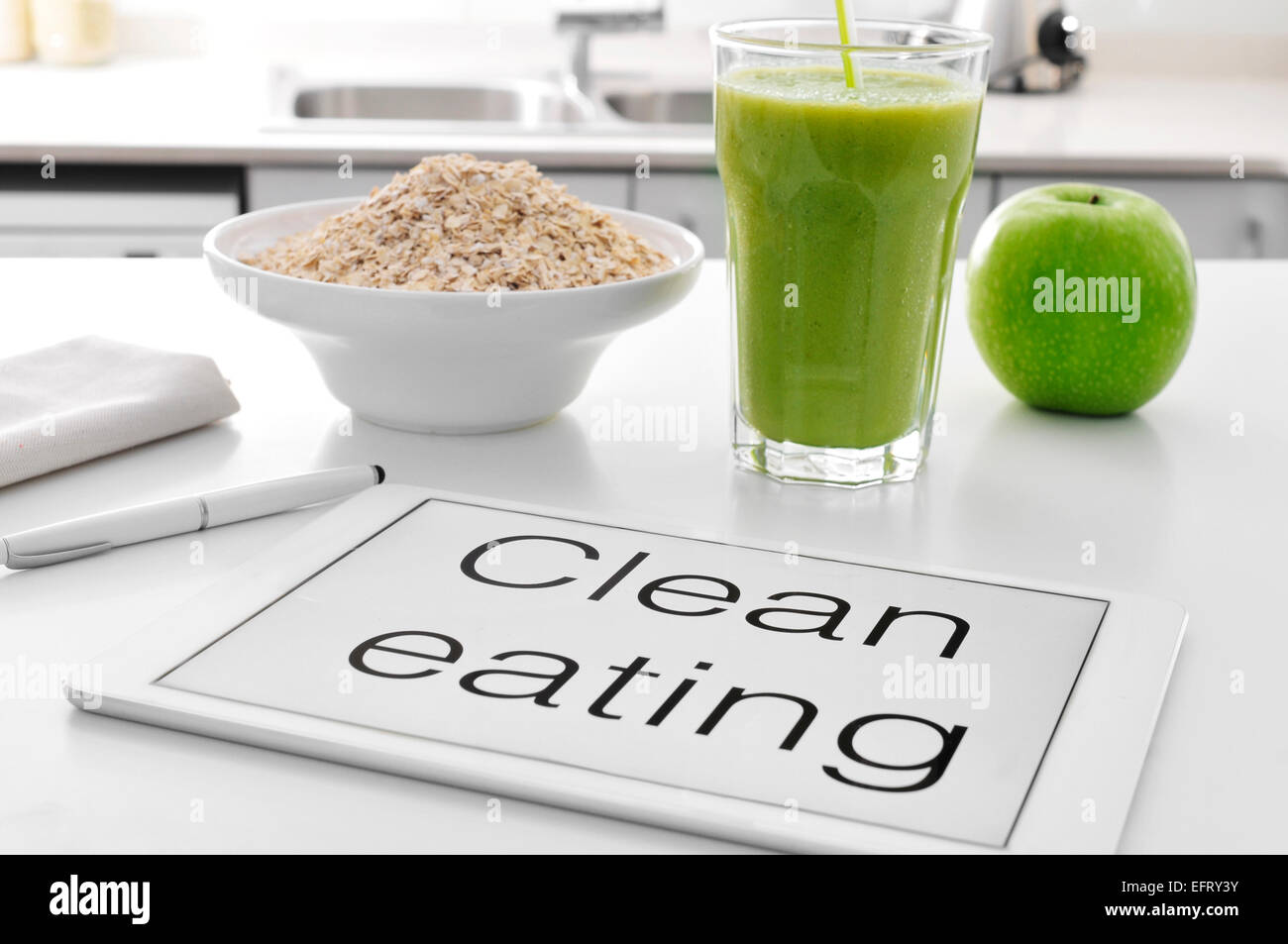 a tablet with the text clean eating written in it and a bowl with oatmeal cereal, a glass with a green smoothie and an apple on Stock Photo