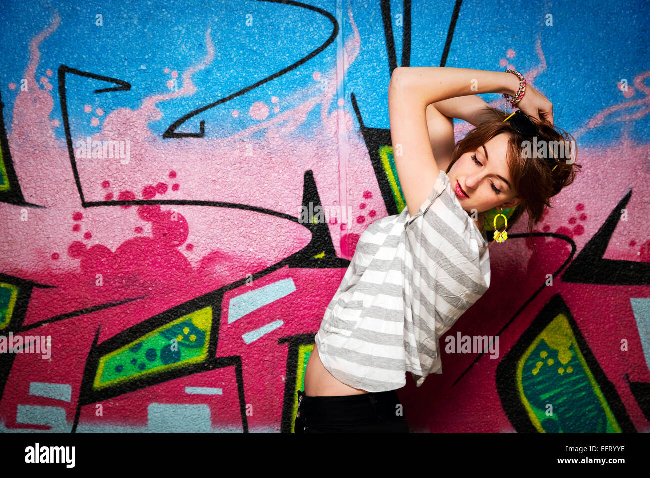Stylish fashionable girl in a dance pose against colorful graffiti wall. Fashion, trends, subculture. Stock Photo