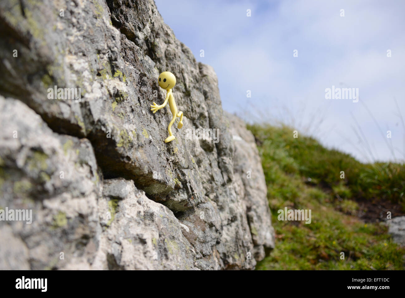 Yellow Smiley Man on holiday in the Outer Hebrides - Here he's rock climbing again in the sun on Eriskay Stock Photo