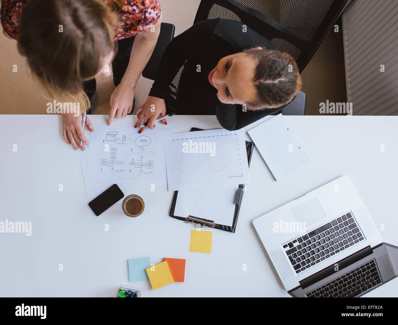 Top view of two young woman working together on a new business project. Businesswoman working on a document at desk in office. Stock Photo