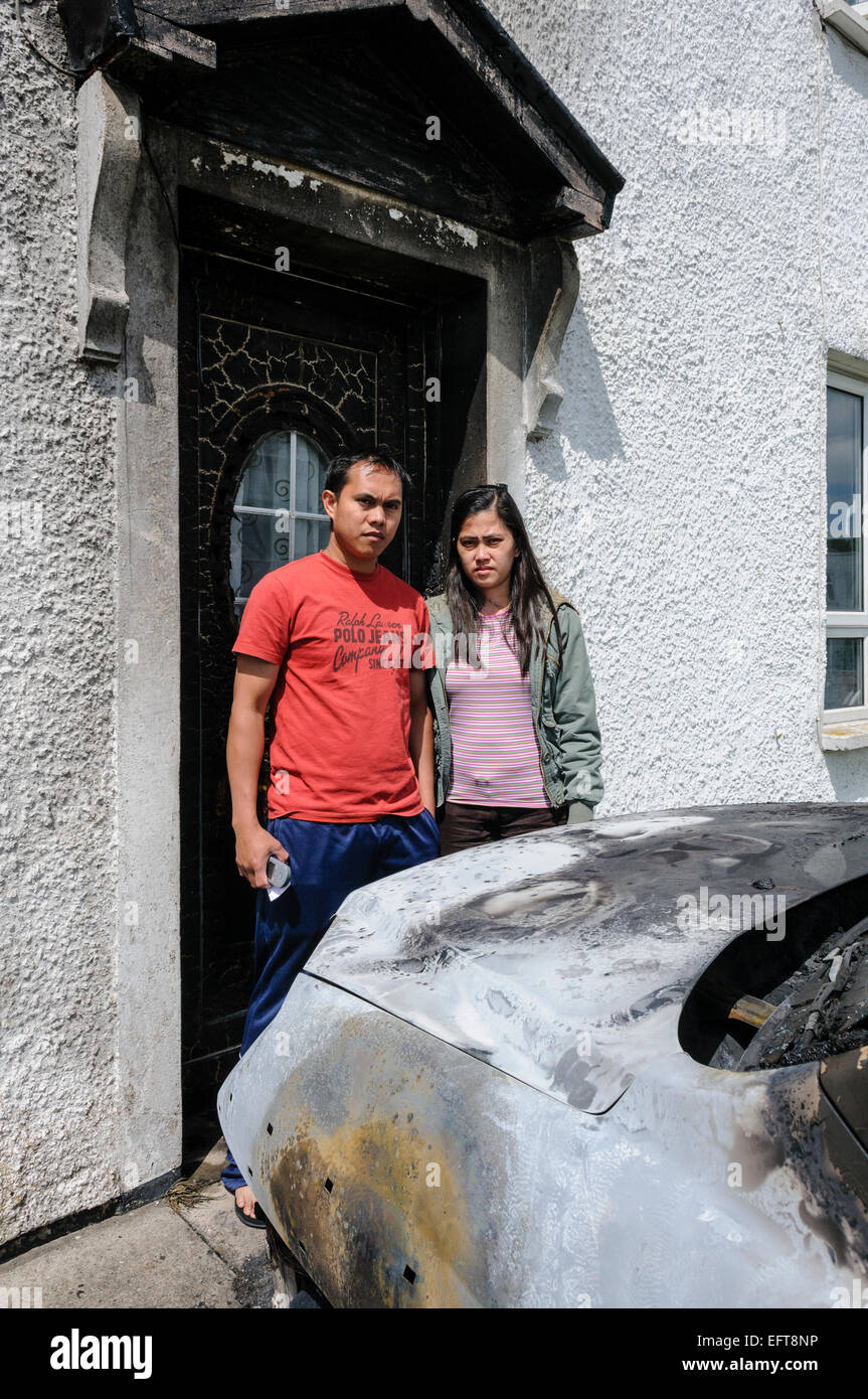 Belfast, Northern Ireland. 22 Jun 2010. An Indonesian couple stand in front of their door following a racist and sectarian petrol bomb attack.  Their car was also destroyed. Stock Photo