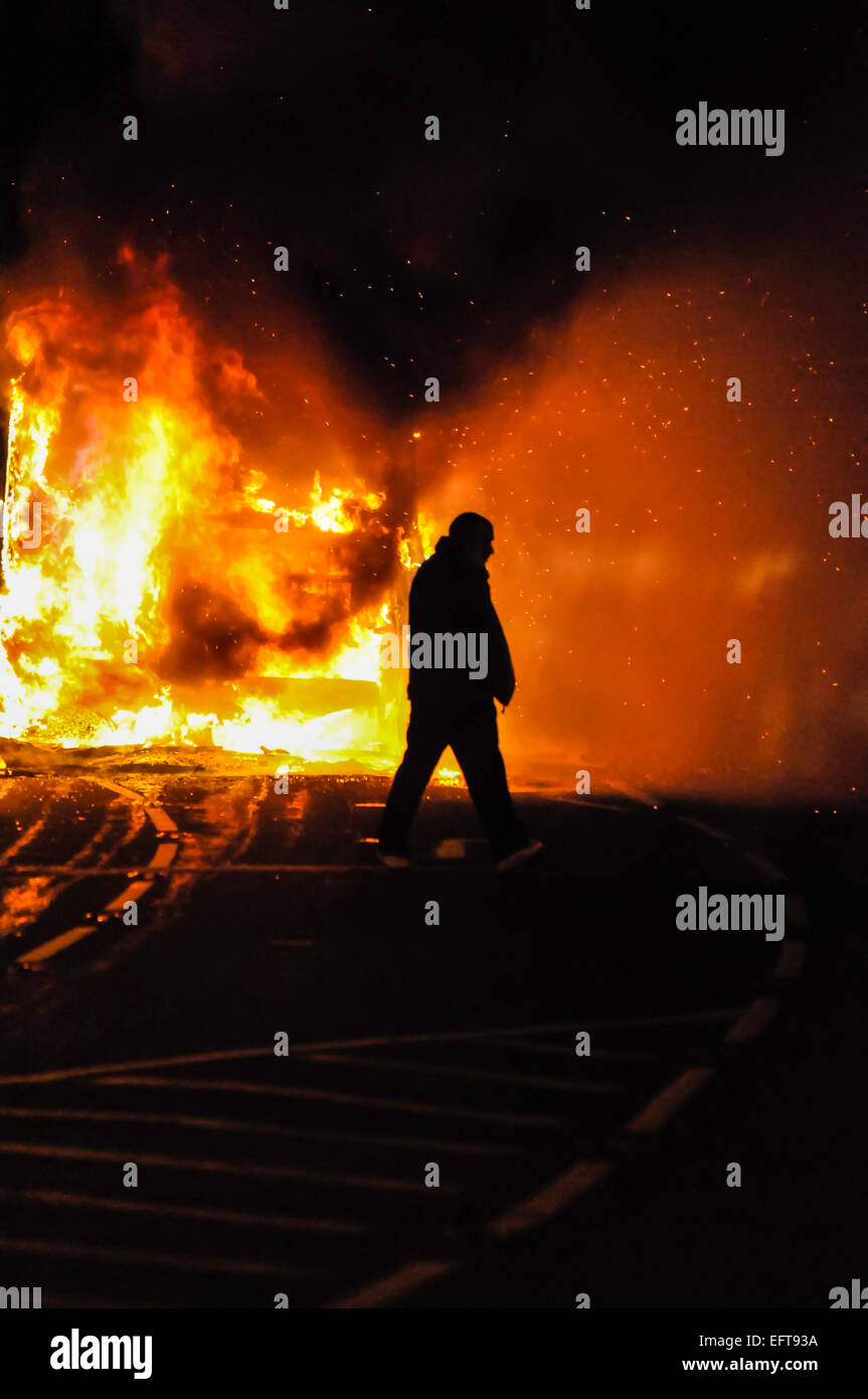 A man walks in front of a burning bus, after forcing the driver off it, and setting it on fire. Stock Photo