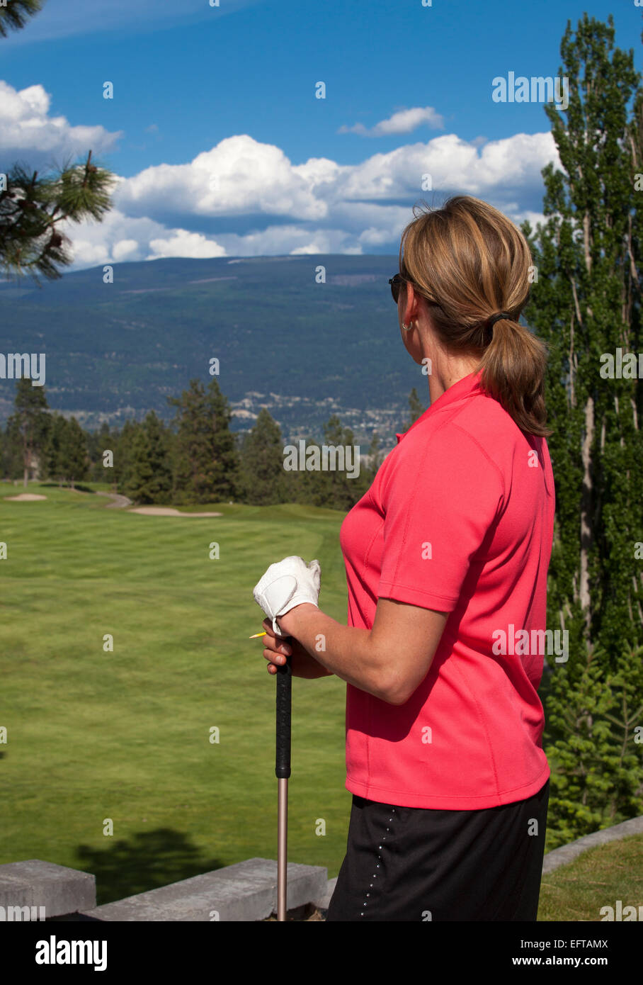 Outdoor photo of female golfer looking at golf course, facing away from camera. Stock Photo