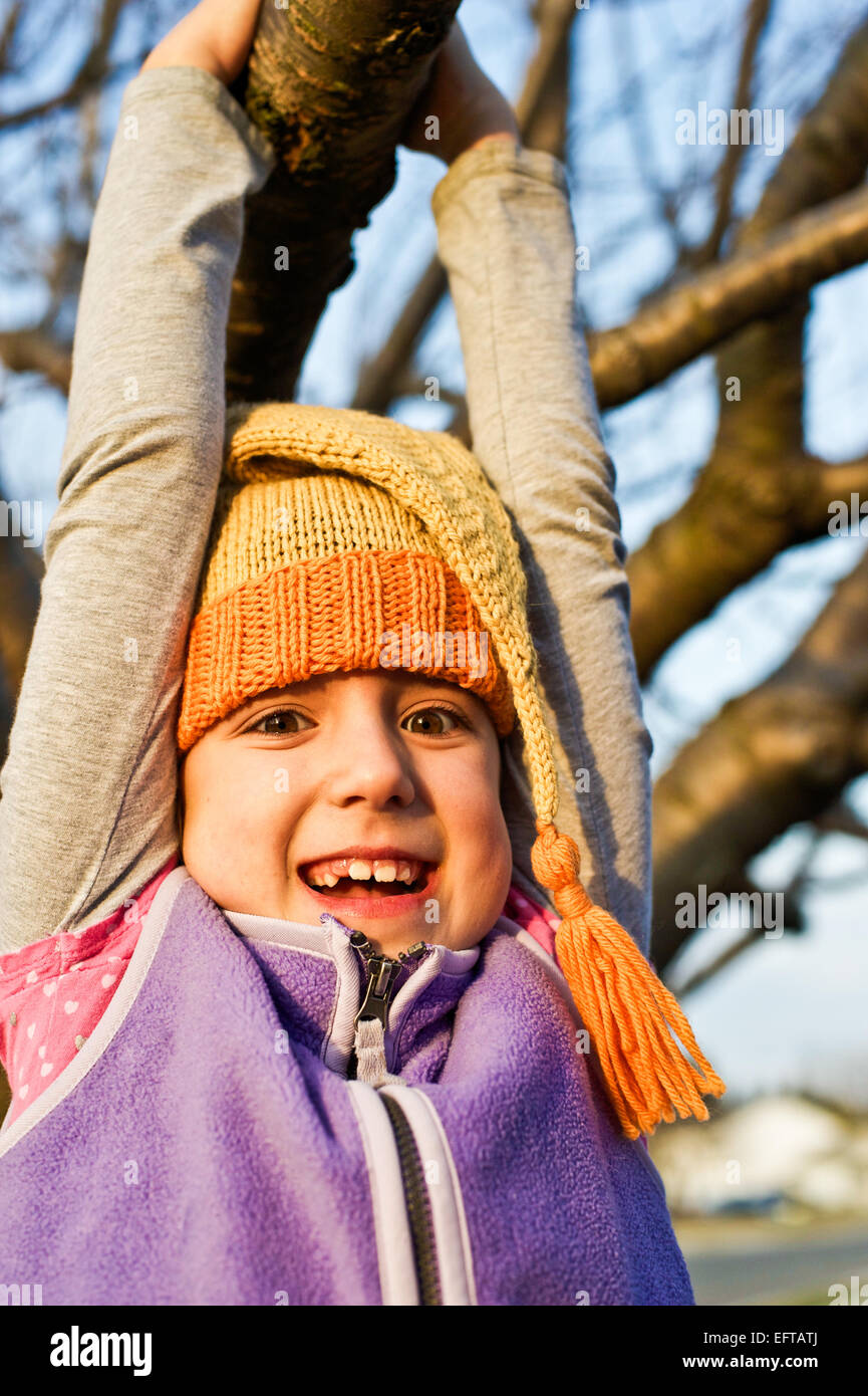 Young girl swinging on a tree branch in the autumn wearing knitted stocking cap. Stock Photo