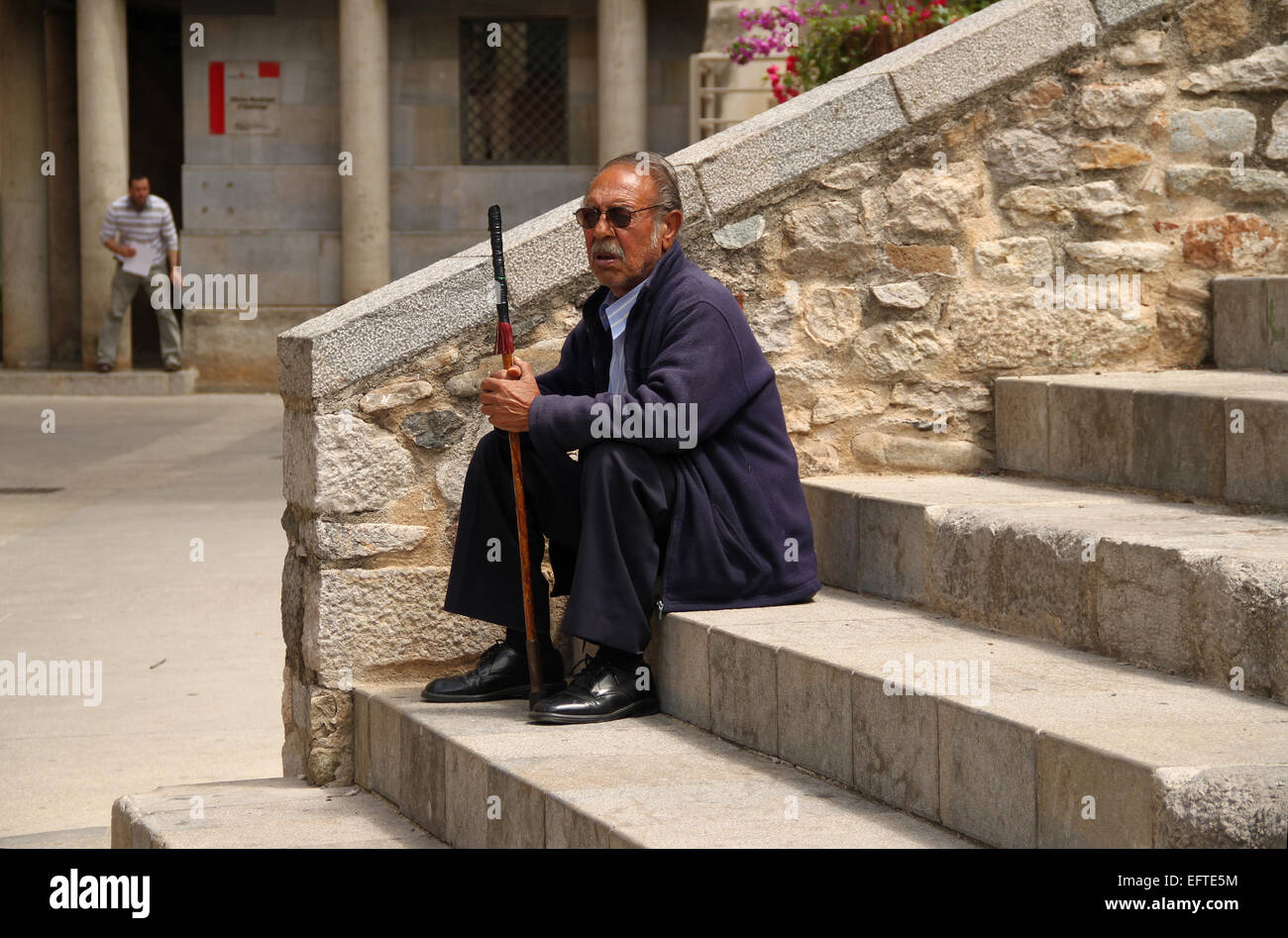 Old man sitting with walking stick on steps in old town of Girona (Gerona), Catalonia, Spain Stock Photo