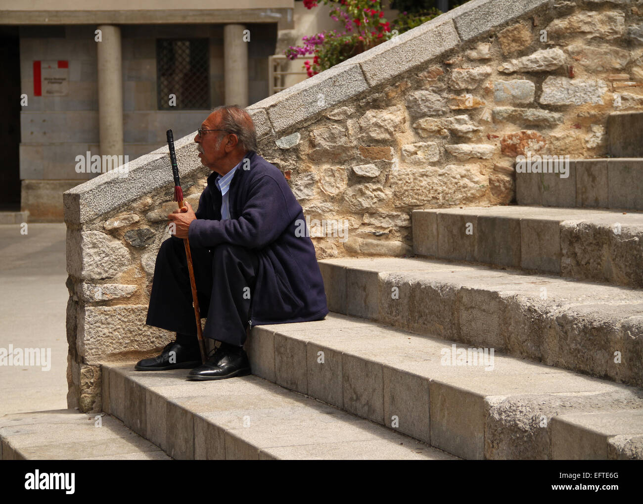 Old man with walking stick sitting on steps in old town of Girona (Gerona), Catalonia, Spain Stock Photo