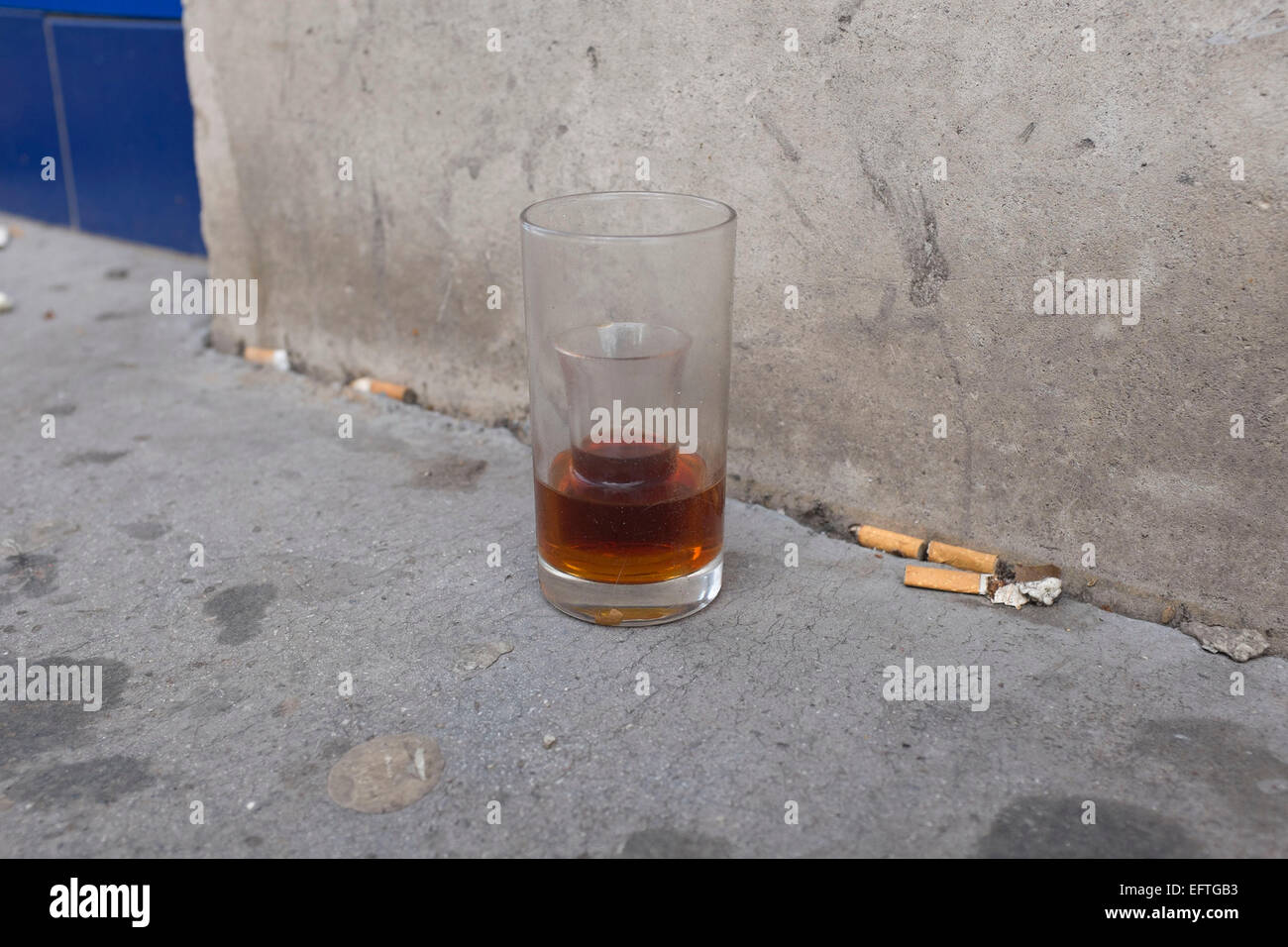 Sign of a big night out. A shot glass inside another glass and some cigarette stubs. Possibly the remnants of a Jager Bomb or a depth charge, where two drinks mix into one glass. Stock Photo