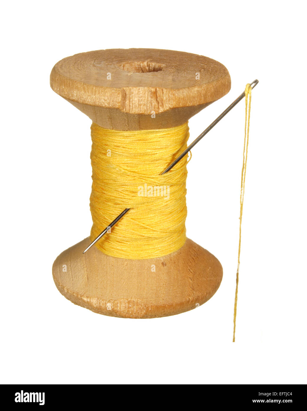 Old wooden spool of yellow thread and needle isolated on white background. Stock Photo