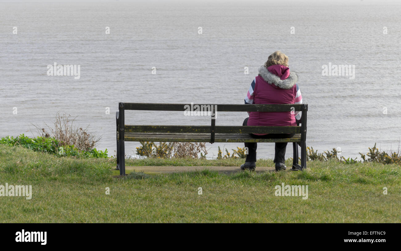 woman sitting on a bench looking out to sea UK Stock Photo