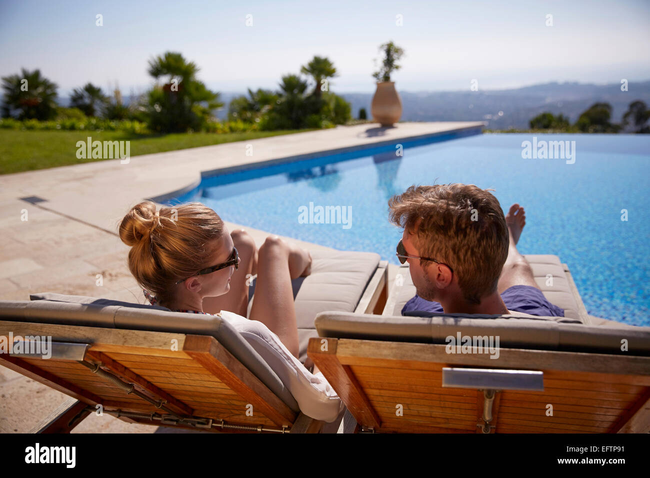 Couple on holiday on sun loungers by a villa pool looking over the Cote d’Azur Stock Photo