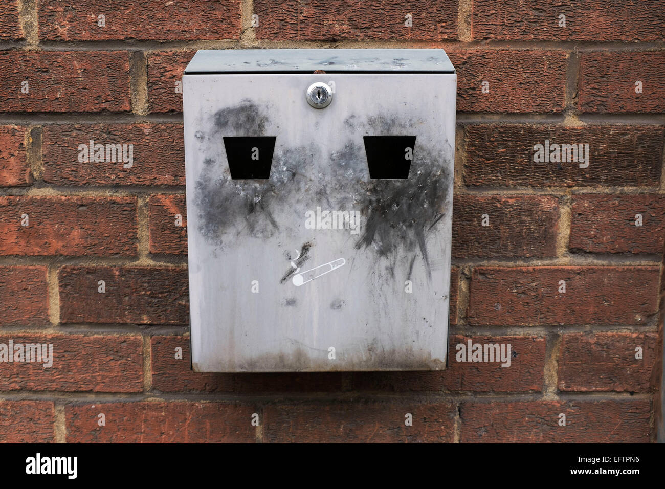 Ash tray which looks like a face on a wall outside. London, UK. Since the smoking ban in public places, these ashtrays have become a common sight as smokers go out to smoke. Stock Photo