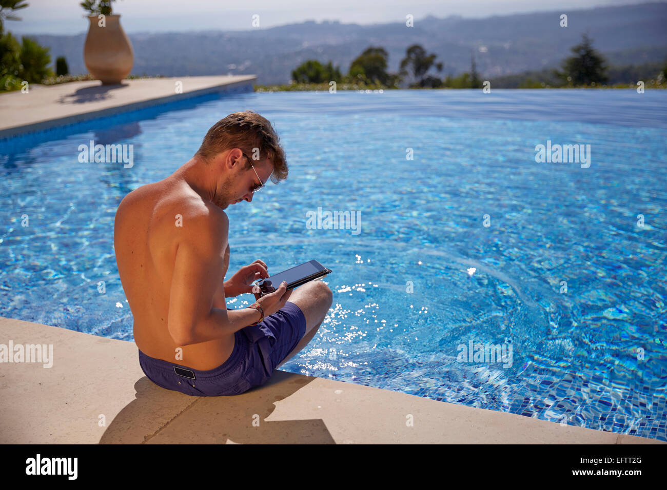 Young man by the pool on holiday with a tablet computer Stock Photo