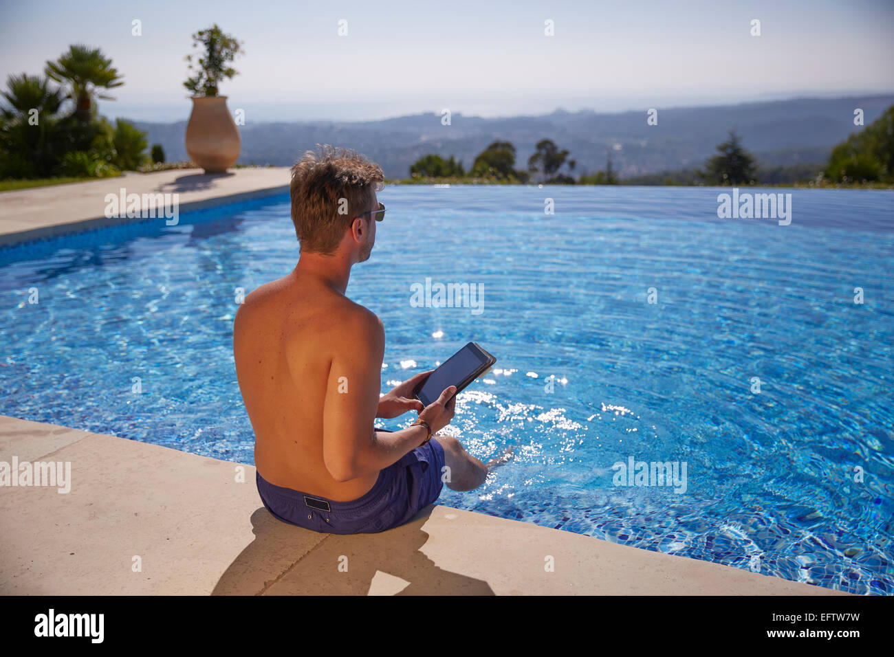 Young man by the pool on holiday with a tablet computer Stock Photo