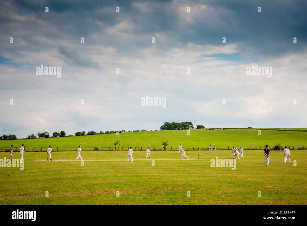 Rural scene with view cricket players playing cricket match on cricket field Stock Photo