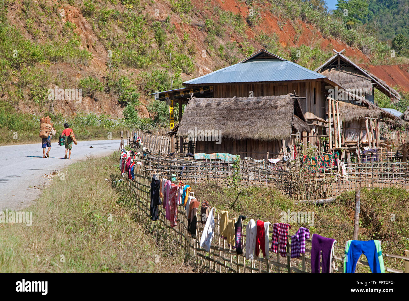 Burmese man carrying firewood on his back and laundry drying on fence in rural village, Tachileik District, Shan State, Myanmar Stock Photo