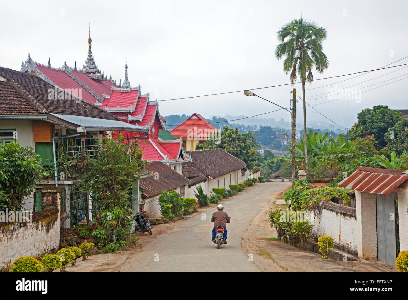 Motorcyclist riding past Buddhist temple in the town Keng Tung / Kengtung, Shan State, Myanmar / Burma Stock Photo