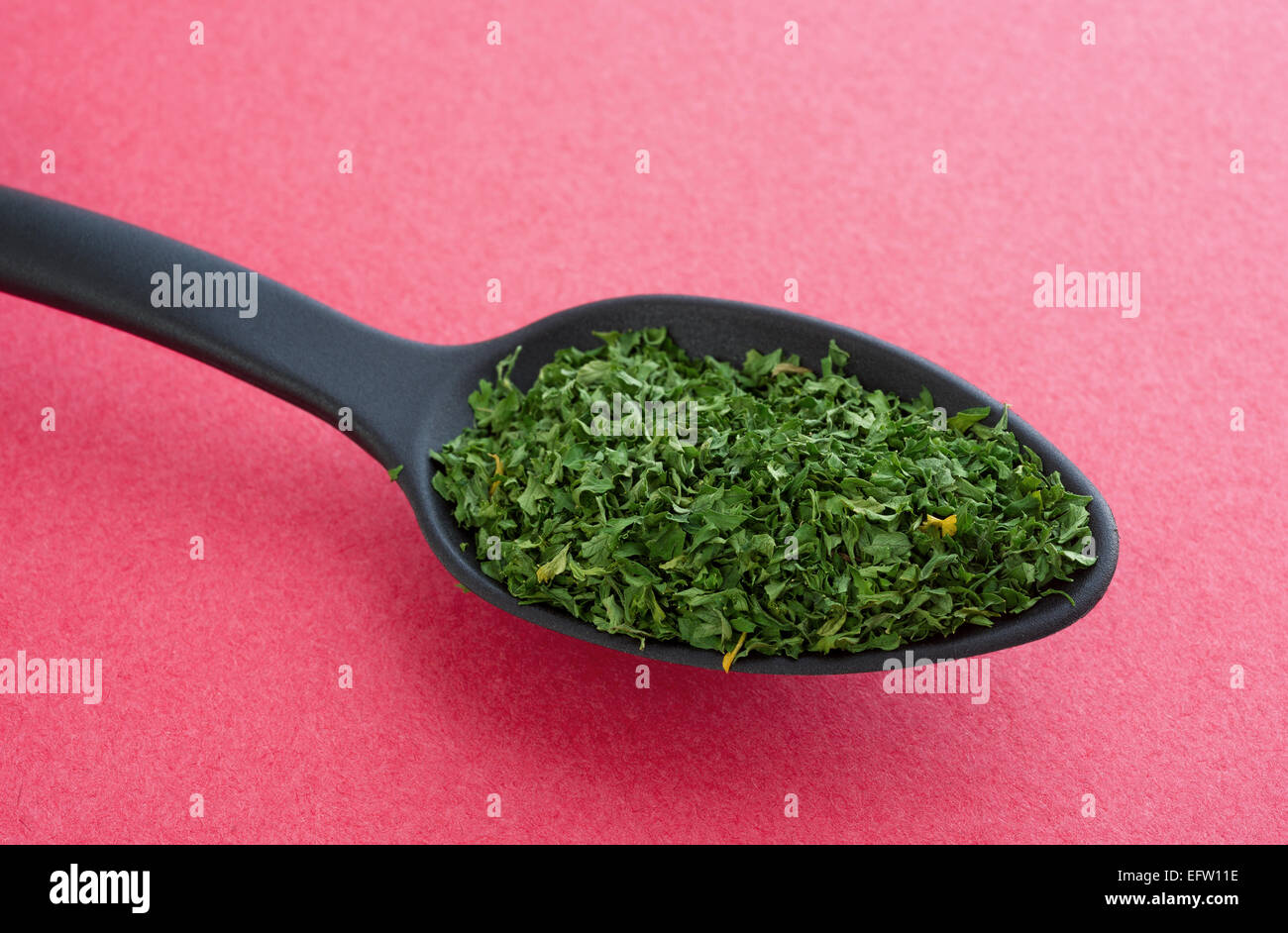 Side view of a portion of dried chopped parsley flakes in a black spoon