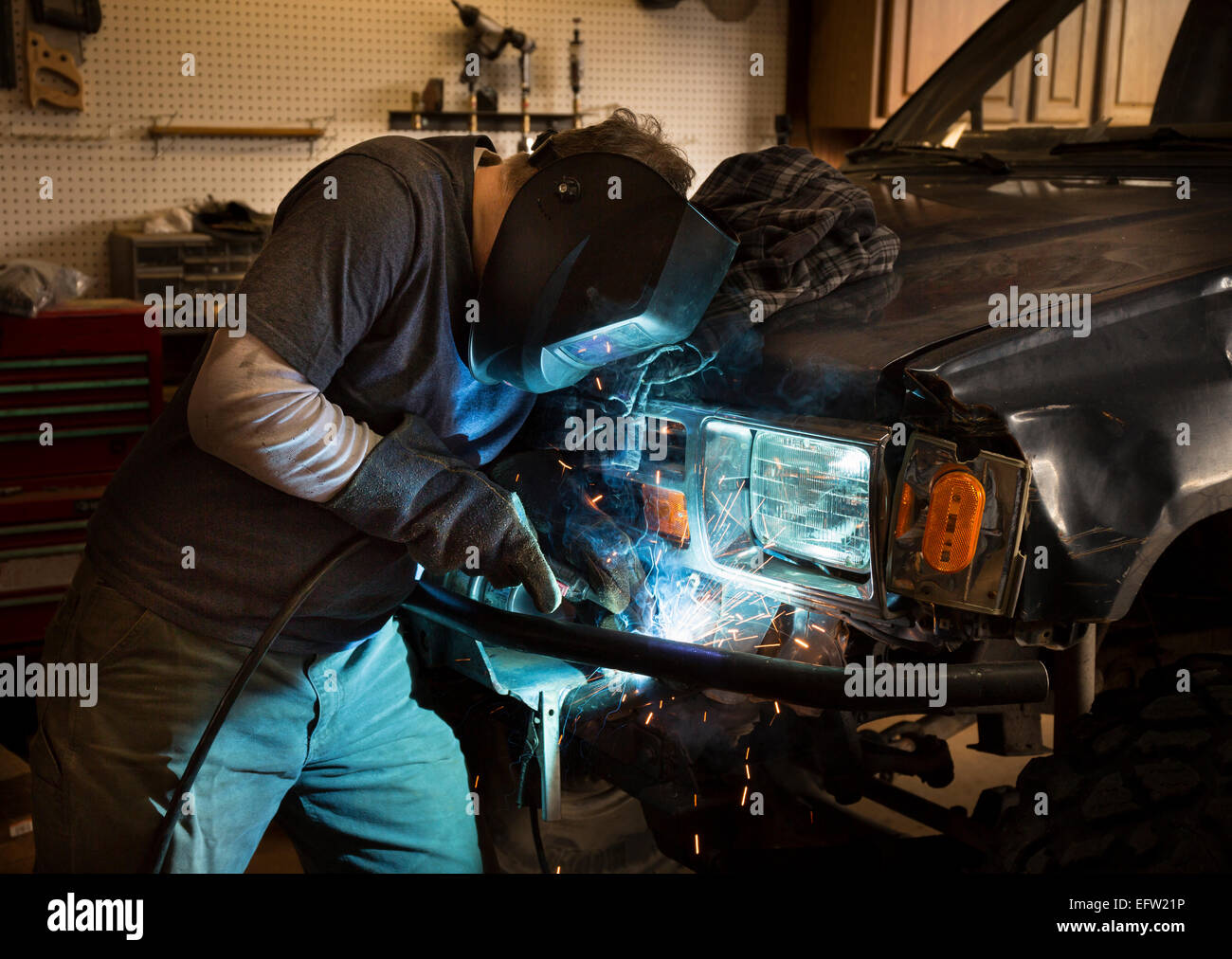 Man wearing welding helmet and welding the bumper of a vehicle Stock