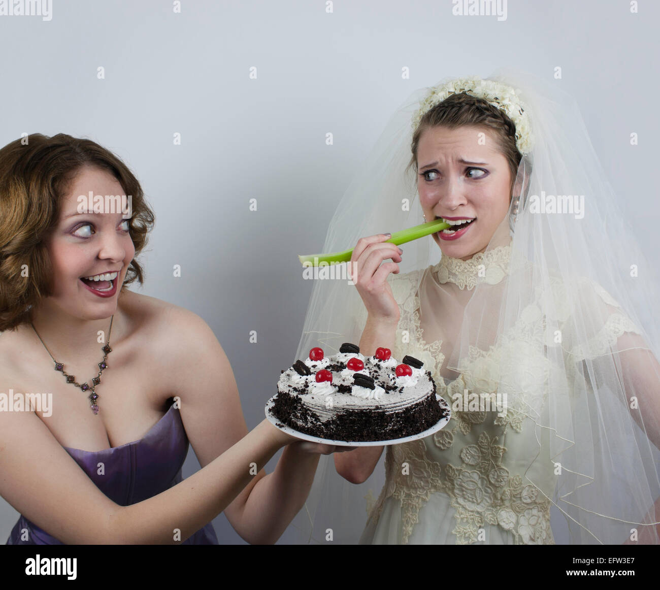 Bride who is trying to diet by eating celery is tempted by a bridesmaid who holds a cake with cherries. Stock Photo