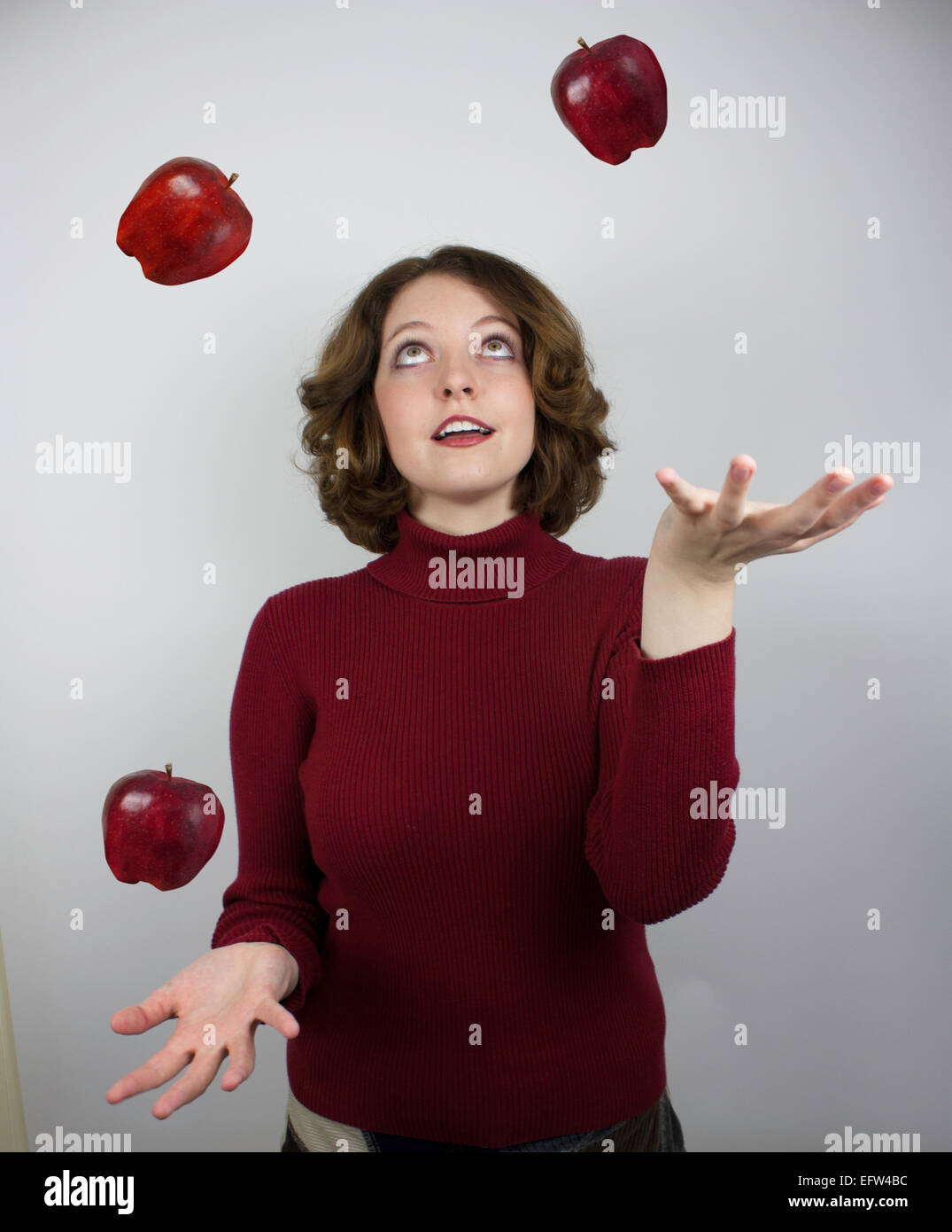 Pretty young woman wearing red sweater juggles apples Stock Photo