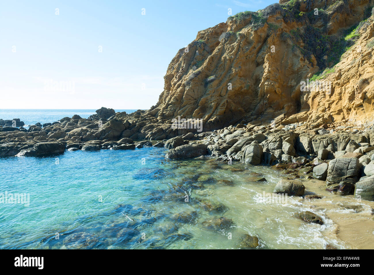 A small, secluded ocean front cove with large, smooth boulders embraces gentle surf bouncing off the large rocks Stock Photo