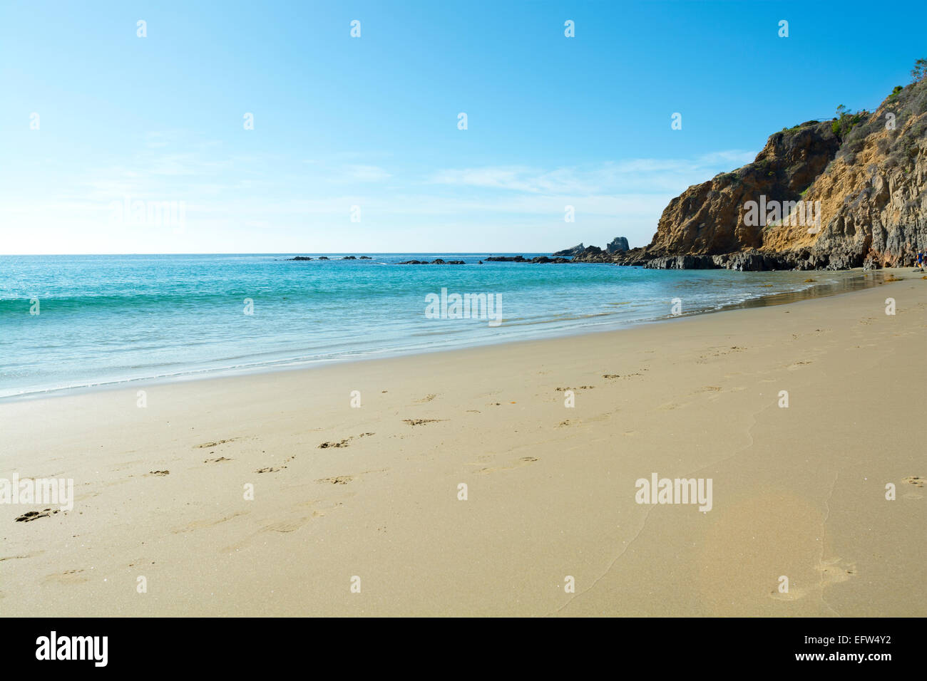 A wide scenic panorama of gently flowing ocean surf against a beautiful sandy beach in a secluded cove in Laguna Beach Stock Photo