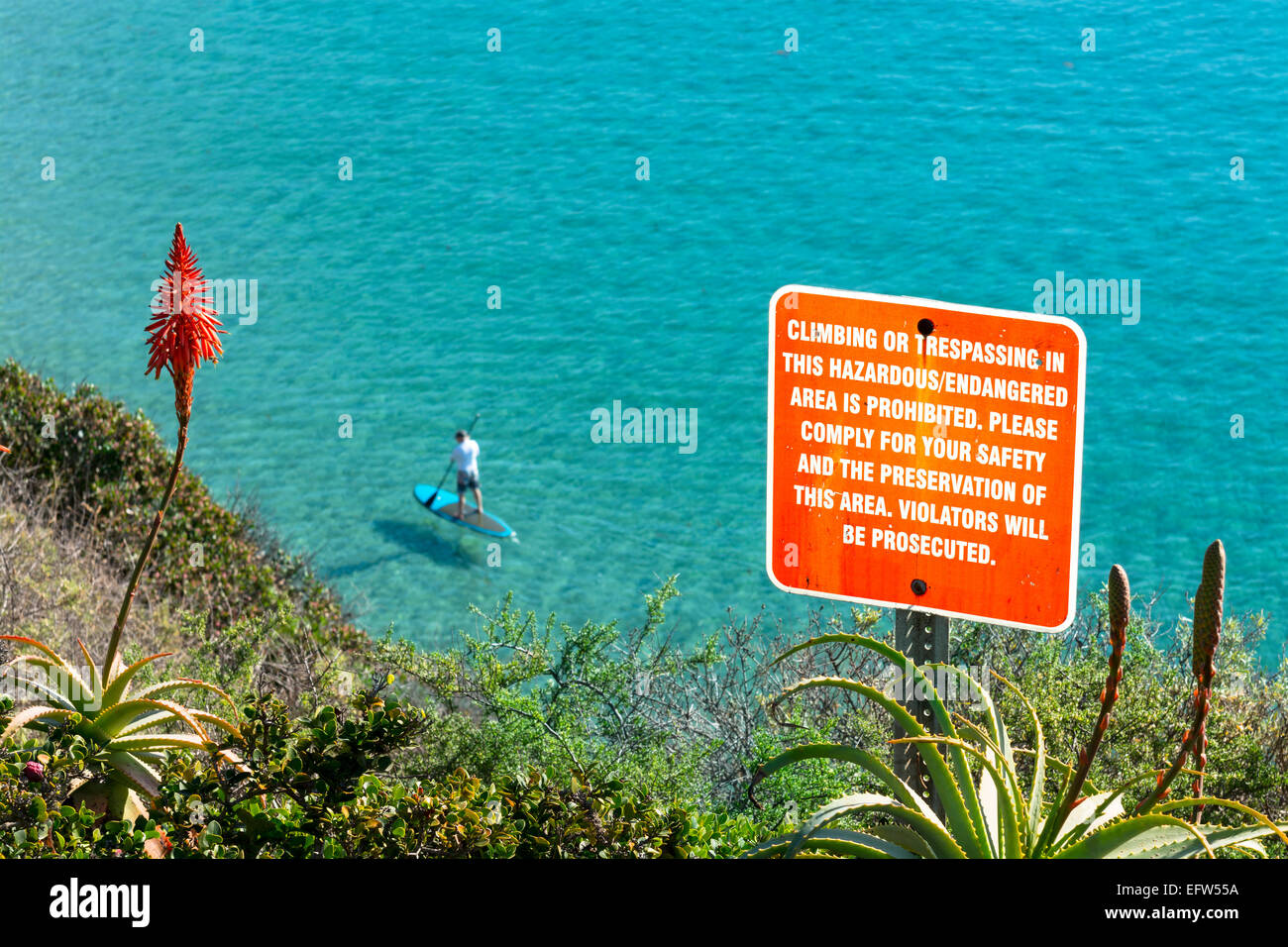 A sign posted on the side of a cliff warning hikers to keep a safe distance from the edge. Stock Photo