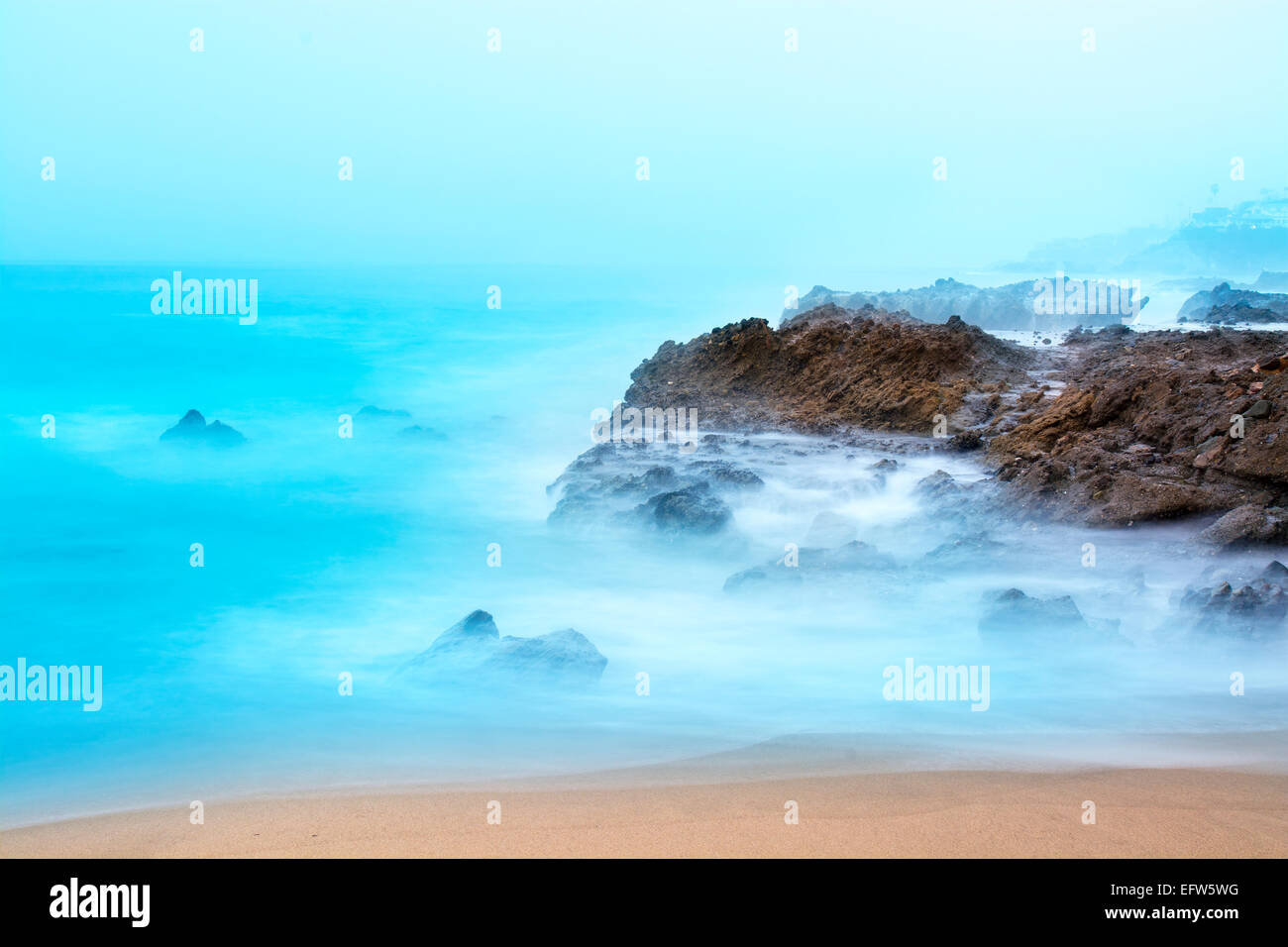 Early morning sunrise cases beautiful light onto a reef where slow shutter speeds capture the motion of the breaking waves. Stock Photo