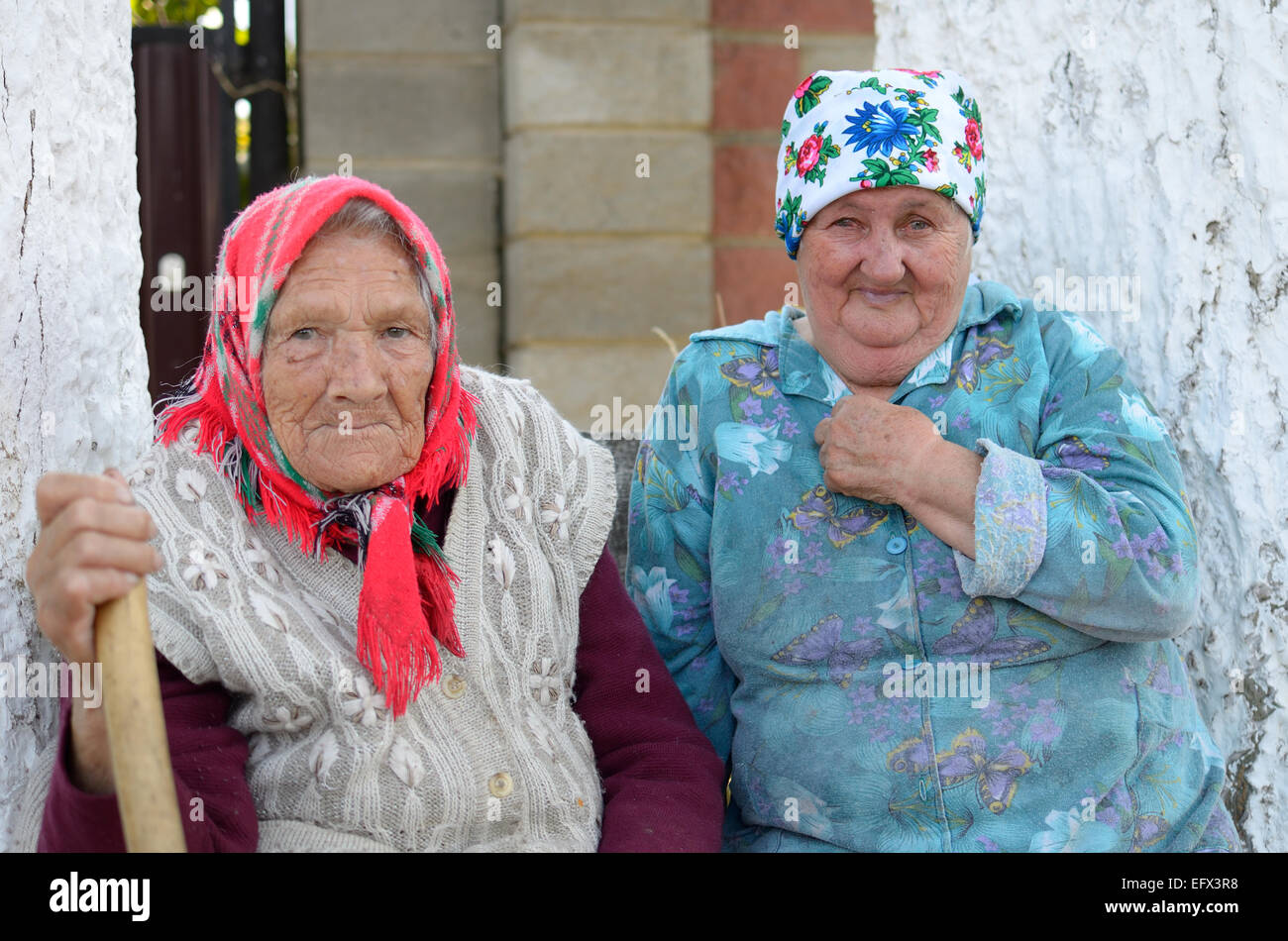 Portrait of two old Russian women sitting near house between two an old poplar trees. Stock Photo