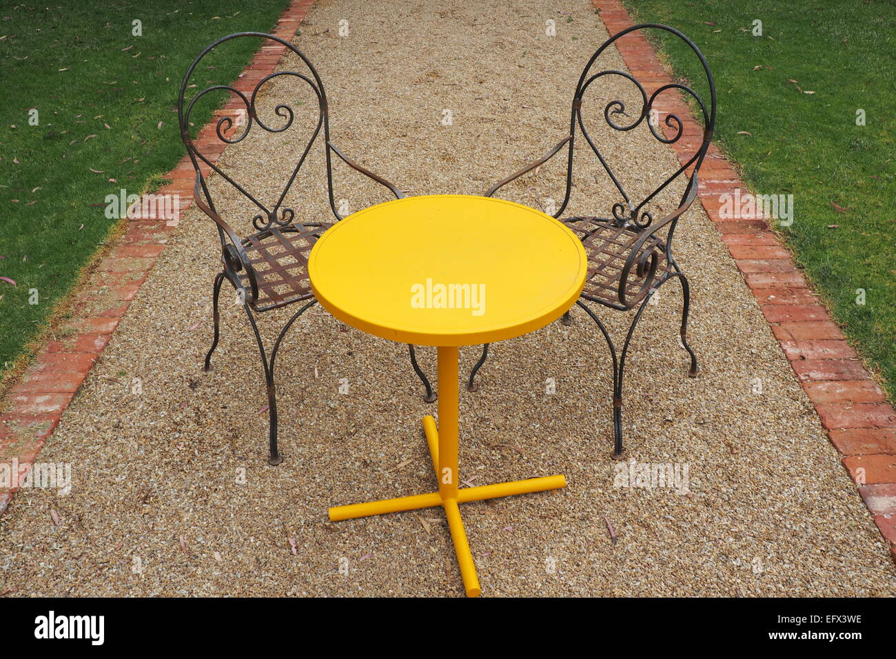 A round yellow table and two metal chairs in a garden Stock Photo Alamy