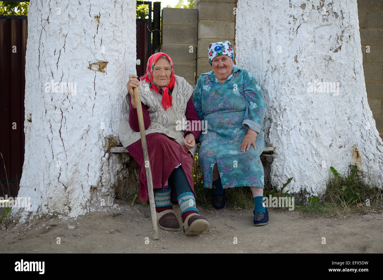 Portrait of two old Russian women sitting near house between two an old poplar trees. Stock Photo