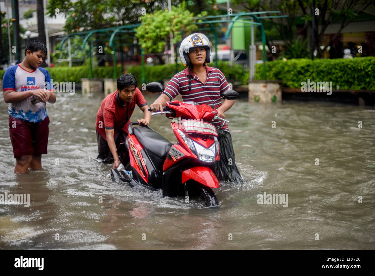 Men pushing motorcycle to pass through floodwaters in Jakarta, after a continuous rain left the downtown area of the Indonesian capital city flooded. Stock Photo