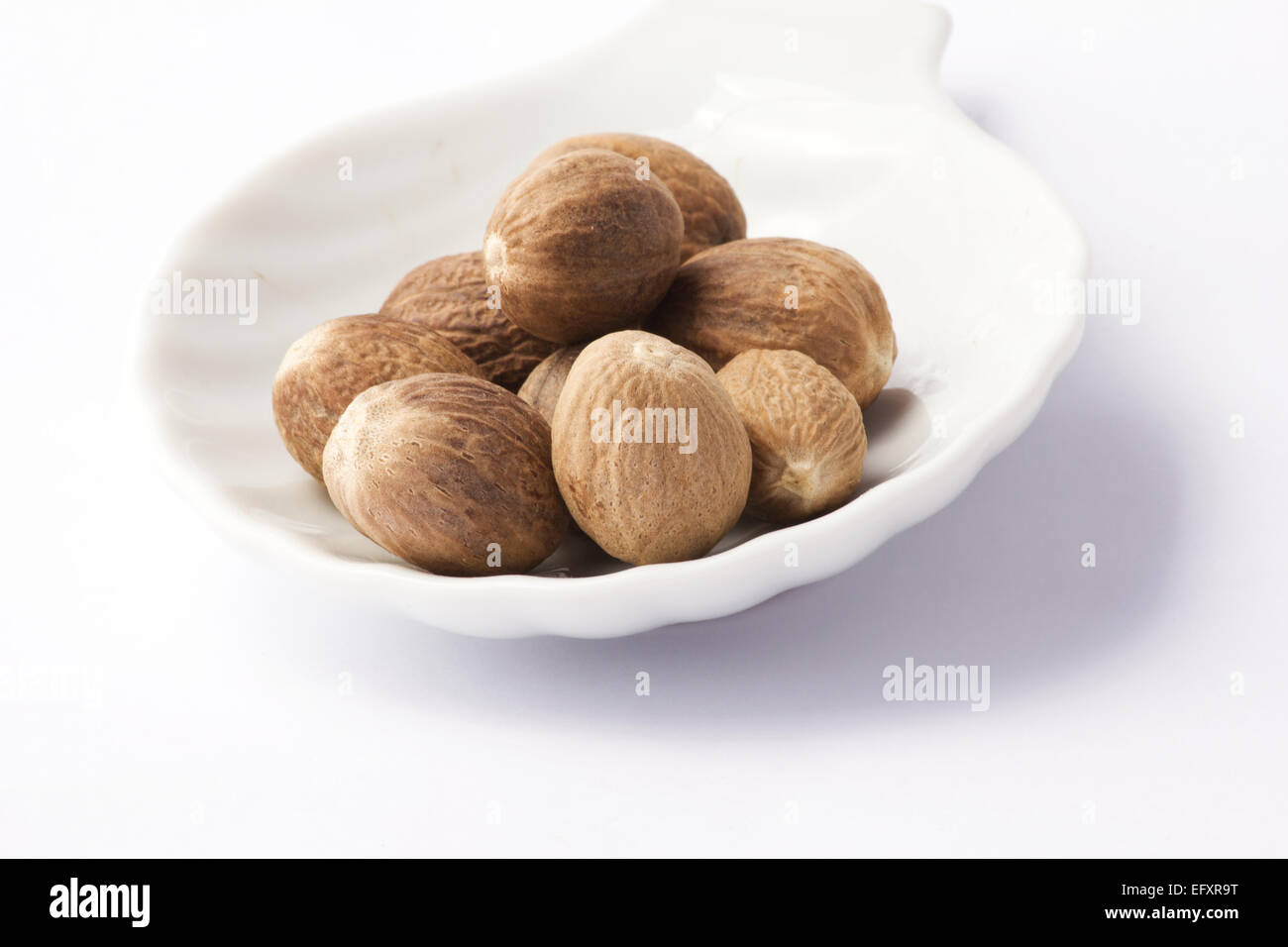 Nutmegs in white bowl on white background Stock Photo