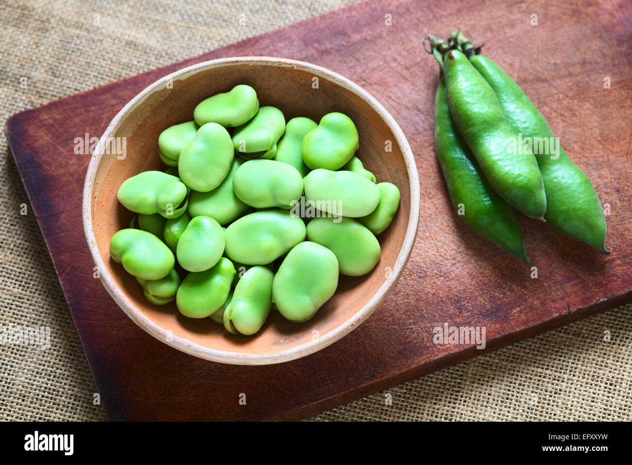 Raw broad beans (lat. Vicia faba) in bowl with pods on the side, photographed with natural light (Selective Focus) Stock Photo