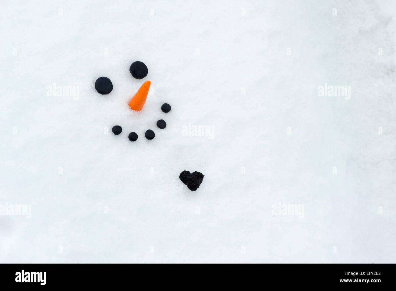 Happy snowman face with a big coal heart in the snow Stock Photo