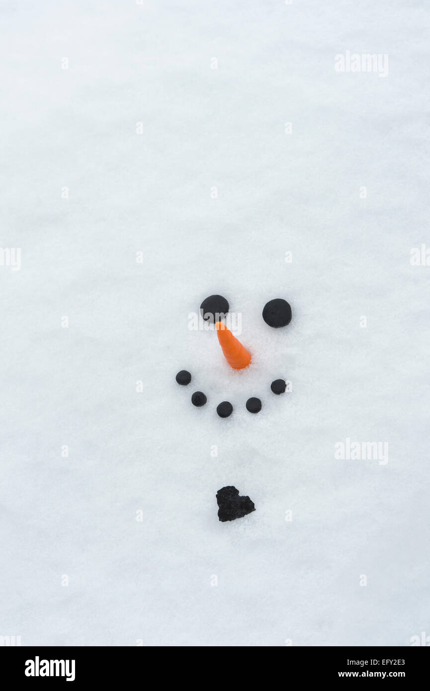 Happy snowman face with a big coal heart in the snow Stock Photo