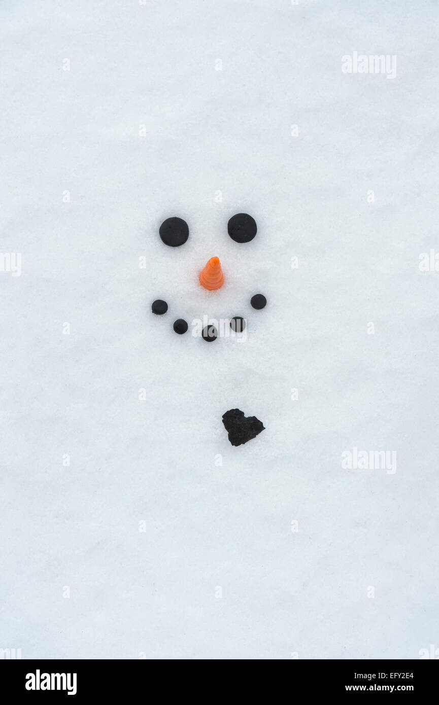 Happy snowman face with a big coal heart in the snow Stock Photo