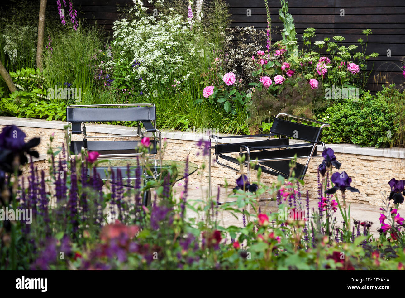 Black leather seats on stone terrace with raised bed made of stones and borders with naturalistic planting Stock Photo