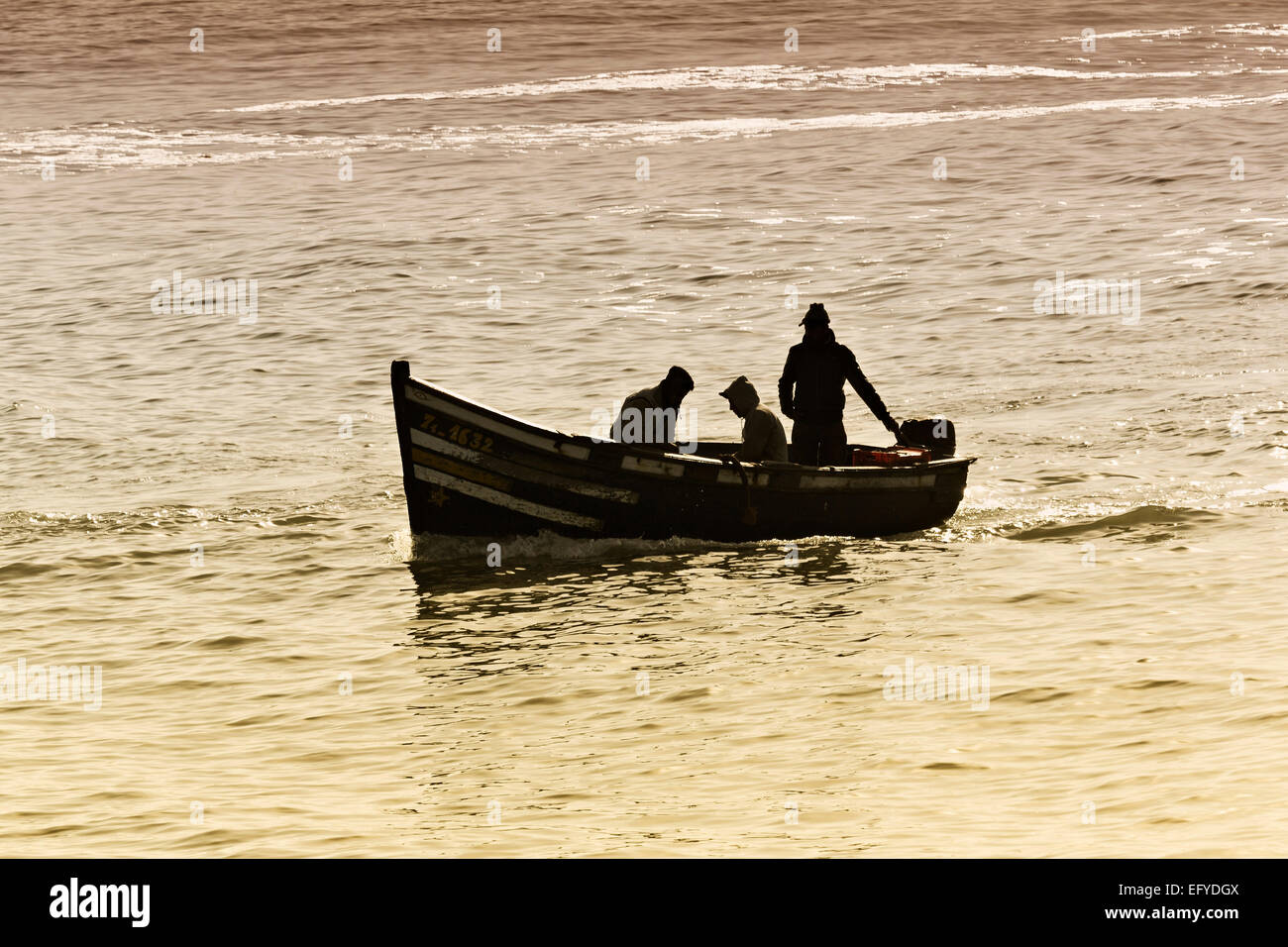 Silhouette von drei Fischern in einem kleinen Boot bei der Einfahrt in den Hafen von Essaouira, Marokko Stock Photo