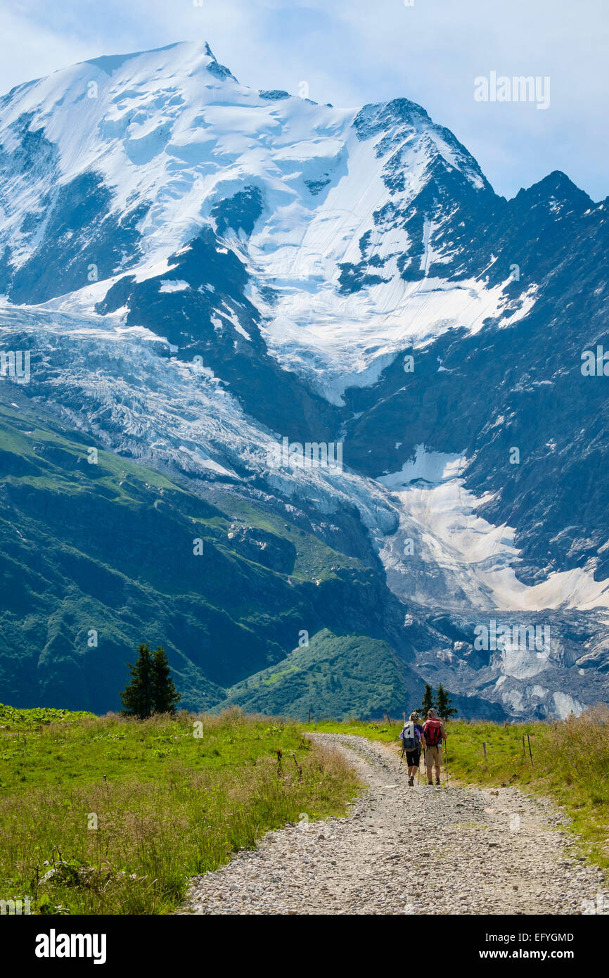 Alps, France - Walkers walking the lower slopes of Mont Blanc and the Glacier de Bionnassay behind, Rhone-Alpes, Haute-Savoie, French Alps, France Stock Photo