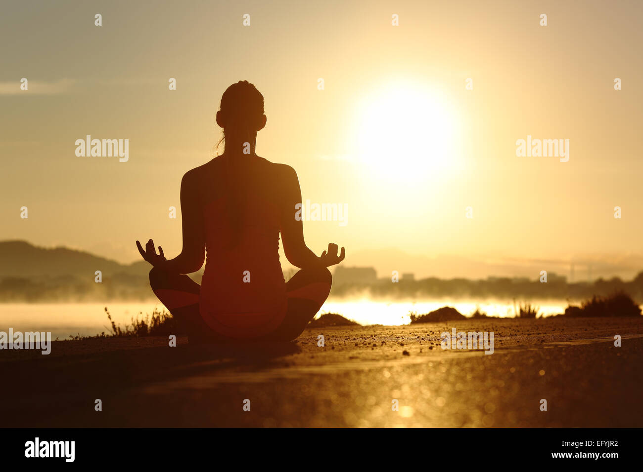 Silhouette of a fitness woman exercising yoga meditation exercises with the sun in the background Stock Photo