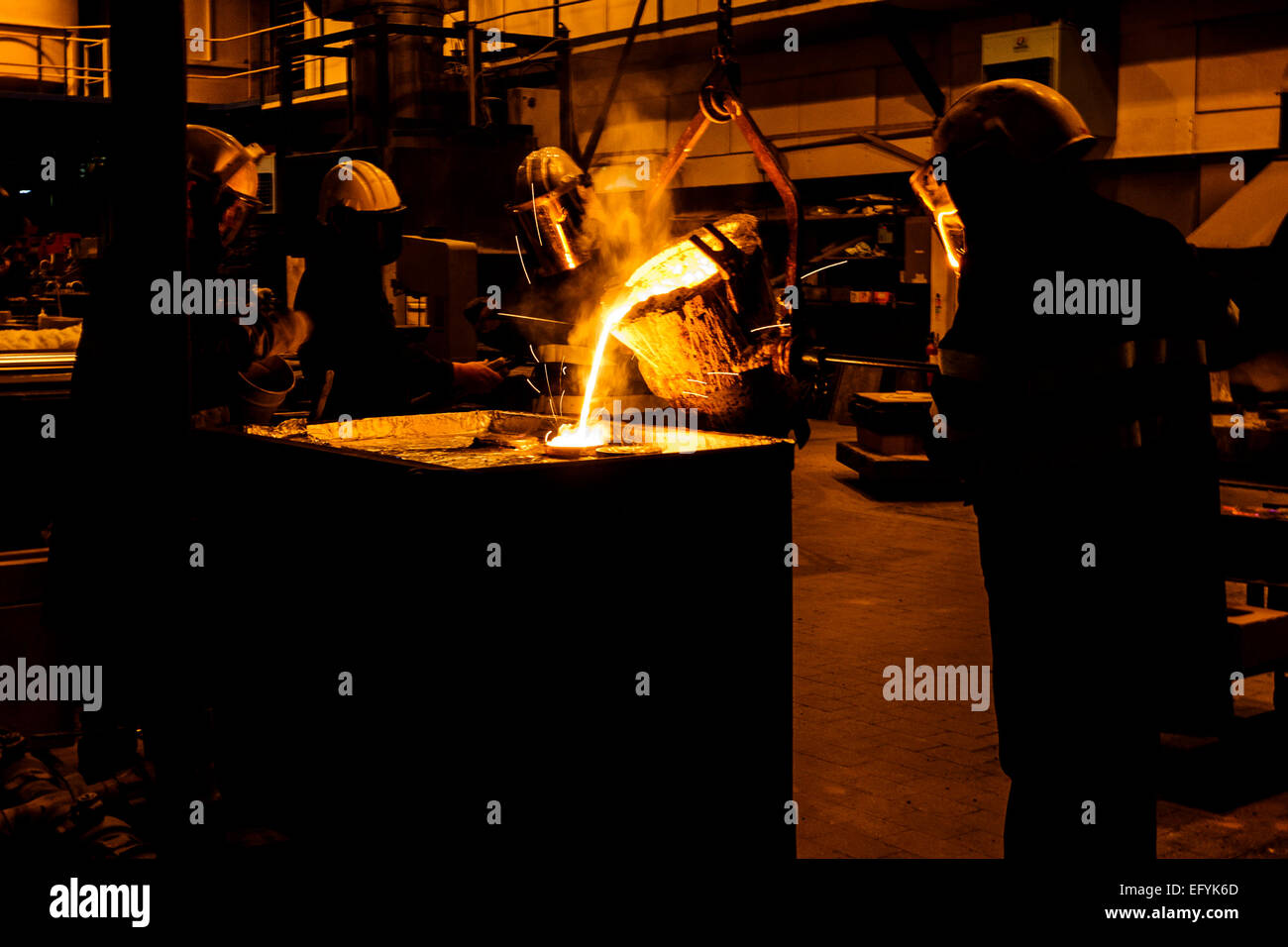 Foundry Working Foundry workers pour molten metal from a furnace using a crucible into ...