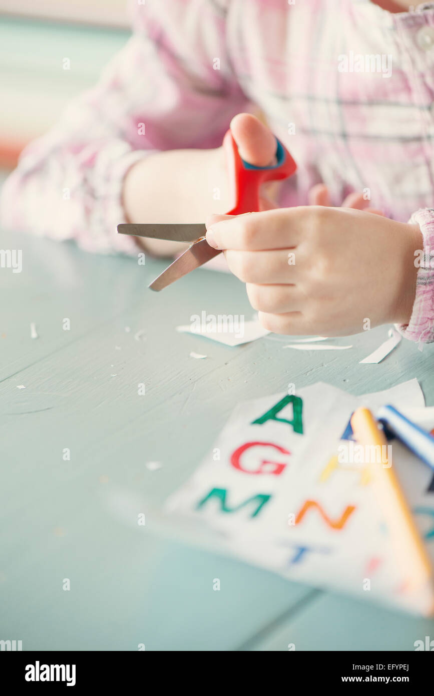 Little girl cutting letters of the alphabet with scissors Stock Photo