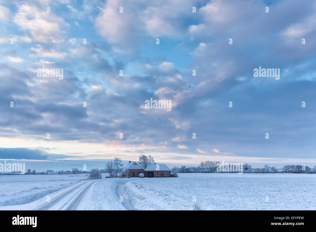 A winter landscape with snow in the fields and a beautiful sky and a farm Stock Photo