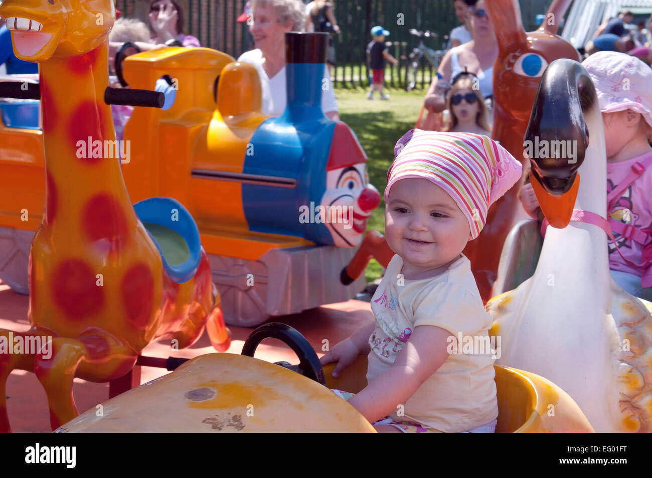 Smiling girl toddler enjoying a ride on a children's merry go round amusement ride at a local village fete. Hempstead Kent UK Stock Photo